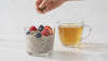 Pumpkin and sunflower seeds sprinkled onto berry chia pudding beside golden herbal tea